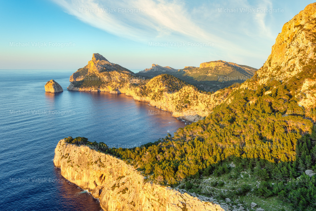 Mirador de Es Colomer auf Mallorca | In der Abendsonne zeigt sich der Blick vom Mirador de Es Colomer mit einer klaren, warmen Lichtstimmung, die die steilen Felswände und die tief eingeschnittene Küstenlinie präzise hervorhebt. Das goldene Licht legt sich gleichmäßig auf die Felsen und betont die Struktur der Landschaft, während das Meer darunter ruhig wirkt und feine Reflexe aufnimmt. Die erhöhte Perspektive öffnet den Blick weit über die Nordküste Mallorcas und vermittelt einen sachlichen, klar gegliederten Eindruck dieses markanten Aussichtspunkts. - Realisiert mit Pictrs.com