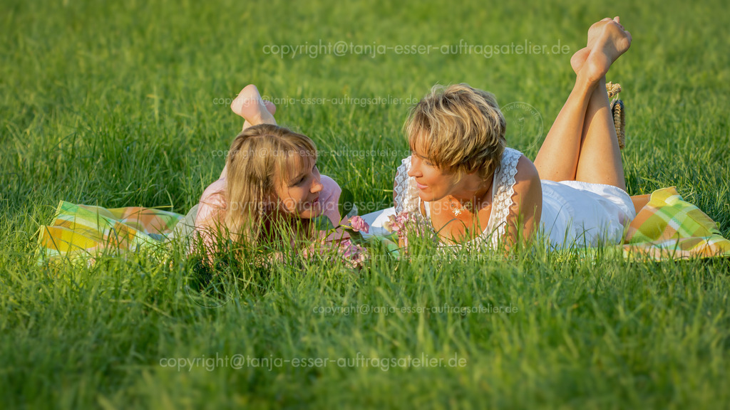 Schwestern picknicken auf Sommerwiese | Zwei Schwestern zwischen 30 und 40 Jahren liegen auf einer Decke in der Natur und reden miteinander. Es ist ein Sommer Nachmittag, die Sonne steht tief. Copy Space. 