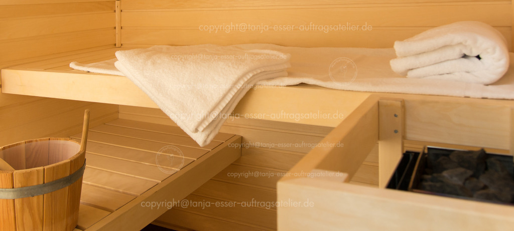 Innenaufnahme einer kleinen Sauna mit Saunaofen und zwei Holzpritschen. | Eine kleine Sauna mit 2 Holzliegestühlen. Kleine Kabine in einem Badezimmer. Saunaofen, Liegestühle, Wasser, Handtücher.