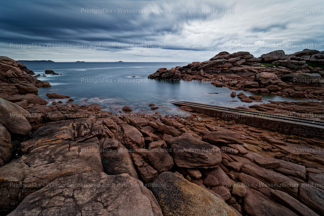 Felsenbucht an der bretonischen Küste | Raue Küstenlandschaft in der Bretagne mit rötlichen Granitfelsen, ruhigem Meer und dramatischem Wolkenhimmel. Die weiche Wasserbewegung und die natürlichen Felsstrukturen verleihen der Szene eine stille, kraftvolle und maritime Atmosphäre. - Realisiert mit Pictrs.com