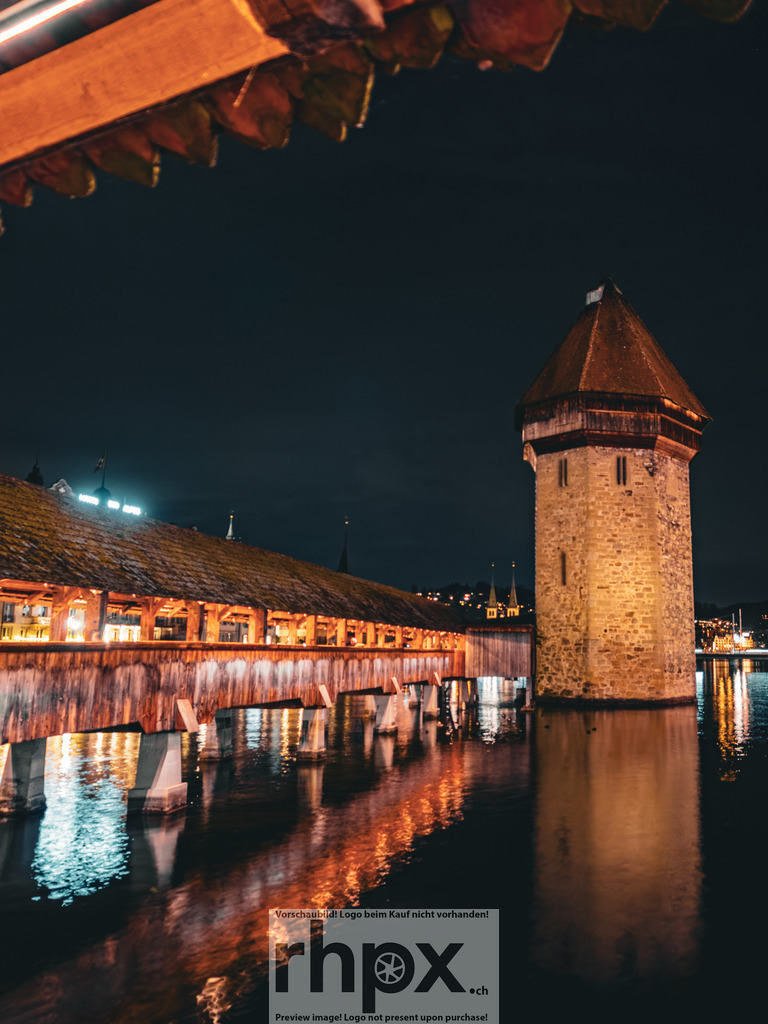 Wasserturm & Kapellbrücke bei Nacht | Holz. Stein. Wahrzeichen.Diese Perspektive fängt die unmittelbare Nähe zwischen den historischen Holzbalken der Brücke und dem massiven Wasserturm ein. Das warme Kunstlicht lässt die Texturen der alten Gemäuer und des Gebälks in der dunklen Luzerner Nacht leuchten.Wähle unter "Produktauswahl" dein Wunschformat: Vom klassischen Wandbild über Puzzle &amp; Tassen bis zum digitalen Download (z.B. als Handy-Hintergrund). - Realisiert mit Pictrs.com