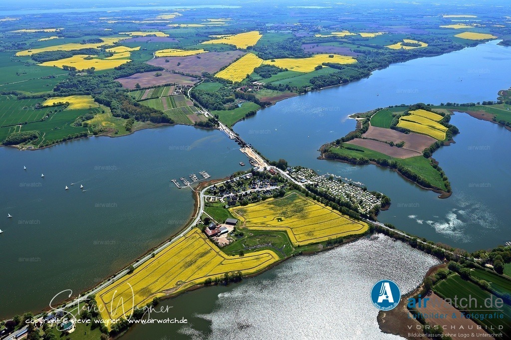 Luftbild Ostseefjord Schlei, Boren-Lindaunis Schleibrücke, Campingplatz Lindaunis, Sportboothafen Lindaunis | Im 19. Jahrhundert war die Region auch durch die Veränderungen im städtischen und landwirtschaftlichen Leben geprägt. Die historische Entwicklung der Gemeinde Boren, die 1974 die Gemeinden Ketelsby und Lindau einbezog, spiegelt die langjährige Entwicklung der Region wider. Die Schlei als natürlicher Grenz- und Verkehrsraum spielte eine zentrale Rolle in der regionalen Geschichte, was auch durch die Erhaltung historischer Gebäude und archäologischer Funde belegt ist.