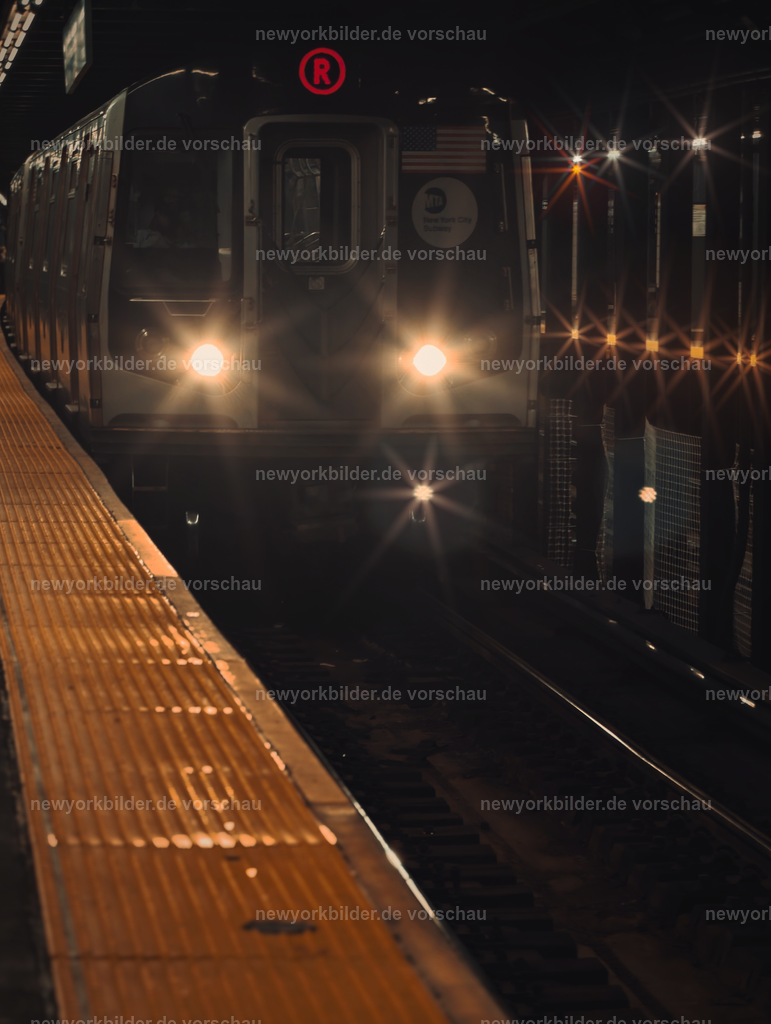 New York City Subway – Einfahrender Zug und die Faszination des Untergrunds | Die Subway ist mehr als nur ein Verkehrsmittel – sie ist ein Wahrzeichen von New York City und ein Spiegel des echten Lebens. Dieses Bild zeigt einen einfahrenden Zug, dessen Scheinwerfer wie Lichtsterne im dunklen Untergrund leuchten. Die Szene ist voller Energie und Kontraste: das metallische Glitzern der Waggons, die warmen Lichtreflexe und die Spannung des Moments, wenn der Zug die Station erreicht. Hier unten gibt es immer etwas zu sehen, zu hören und zu erleben – Musiker, Gespräche, das rhythmische Rattern der Gleise. Trotz aller Herausforderungen bleibt die Subway der schnellste und günstigste Weg, die Stadt zu durchqueren, und sie erzählt Geschichten von Millionen Menschen, die täglich unterwegs sind. Dieses Foto fängt die Essenz von New York ein: roh, lebendig, authentisch. Wer die Metropole liebt, erkennt in diesem Motiv ihre Seele – eine Welt unter der Stadt, die niemals schläft und in der jeder Augenblick ein Stück urbaner Magie ist.