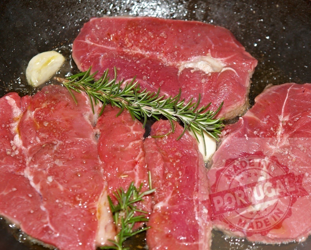 Raw beef steaks cooking with rosemary and garlic | Raw beef steaks seasoning in a hot frying pan with fresh rosemary and garlic - Realized with Pictrs.com