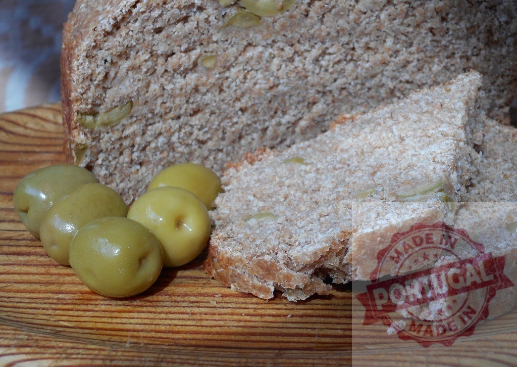 Sliced whole wheat olive bread with green olives on a wooden board | Homemade whole wheat olive bread loaf with fresh green olives on a rustic wooden plate - Realisiert mit Pictrs.com