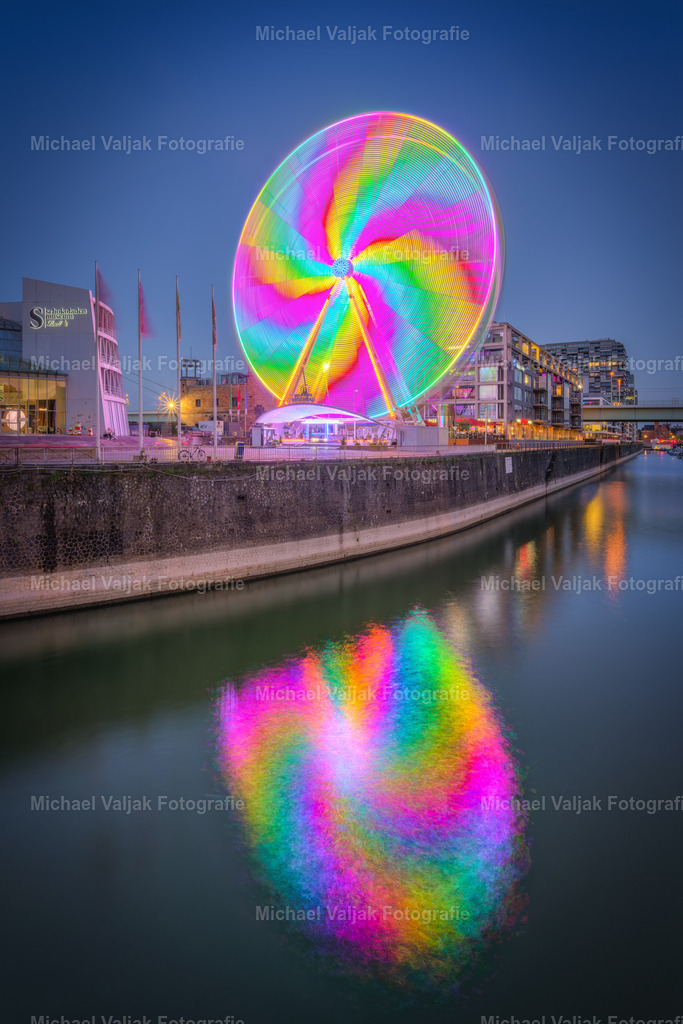 Riesenrad in Köln am Abend | Langzeitbelichtung des sich drehenden Riesenrades auf dem Platz vor dem Schokoladenmuseum in Köln. Durch die wechselnden Lichter und die Lauflichteffekte entsteht durch die Drehung dieser turbinenartige Lichteffekt. - Realisiert mit Pictrs.com
