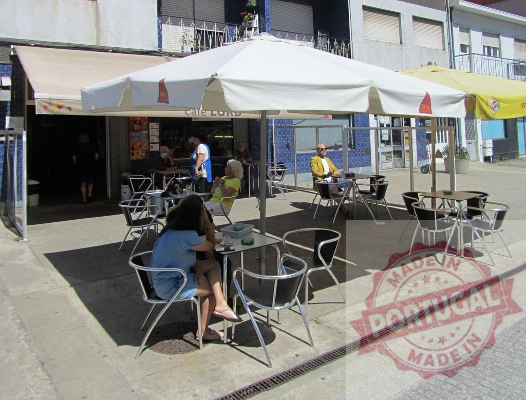 People relaxing at outdoor Cafe LORD terrace on sunny day | Customers enjoying drinks and conversation at a cafe's street side seating area under an umbrella - Realisiert mit Pictrs.com