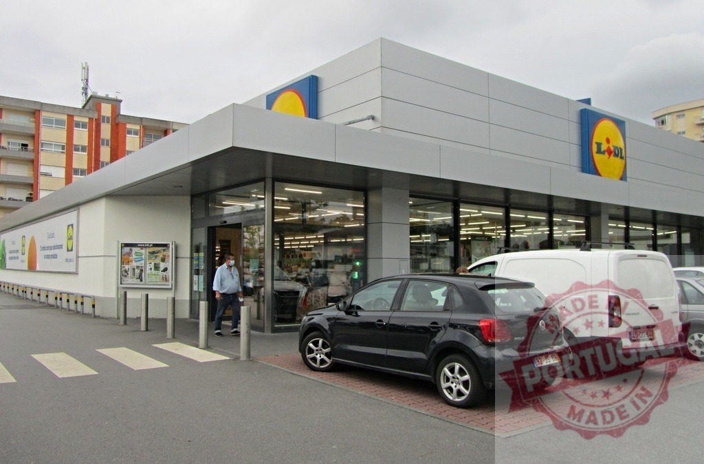 Lidl supermarket building exterior with parking lot and customer | Lidl supermarket building exterior with parked cars and a customer entering the store - Realized with Pictrs.com