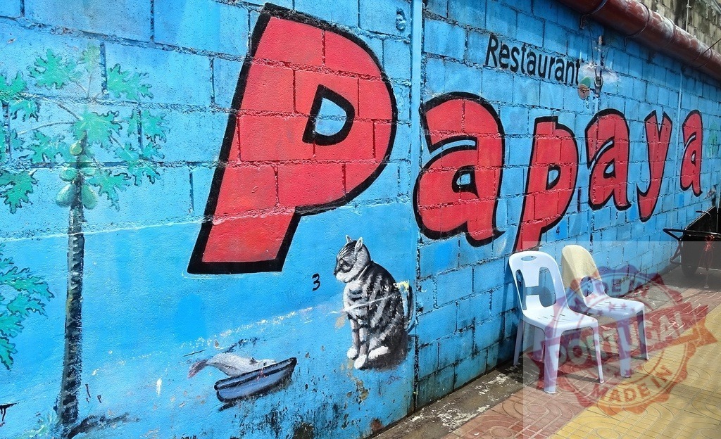 Papaya restaurant sign painted on a blue wall with cat and papaya tree | Vibrant mural advertising Papaya Restaurant, featuring a cat, papaya tree, and a boat on a textured blue wall - Realized with Pictrs.com