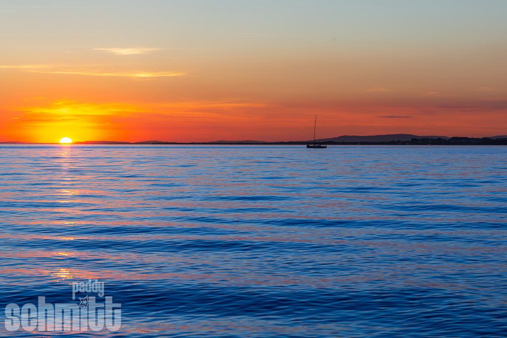 Sonnenuntergang mit Segelboot am Bodensee | Die untergehende Sonne taucht den Bodensee in warme, goldene Farben, während ein Segelboot ruhig über das Wasser gleitet. Die Kombination aus sanftem Abendlicht, weiter Seelandschaft und dem eleganten Segelboot schafft eine zeitlose und stimmungsvolle Aufnahme. - Realisiert mit Pictrs.com