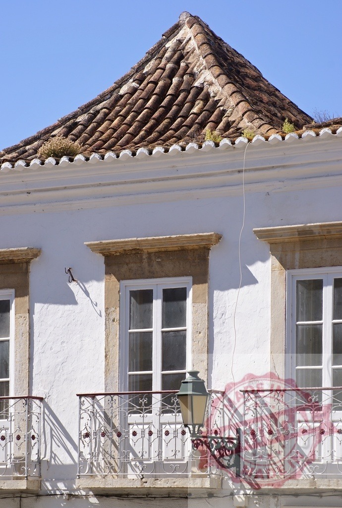 Tavira building facade featuring balcony and traditional roof tiles | Old building showcasing traditional architecture with balconies, a streetlamp, and unique roof tiles - Realized with Pictrs.com