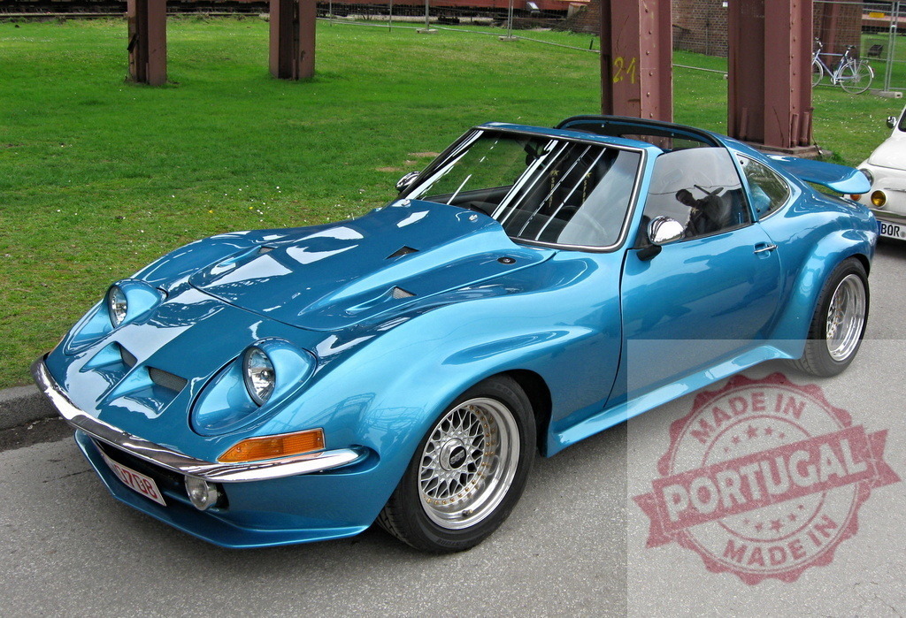 Shining blue Opel GT sports car parked near green lawn | Customized Opel GT parked near a green lawn, showing its shiny blue paint and chrome details - Realized with Pictrs.com