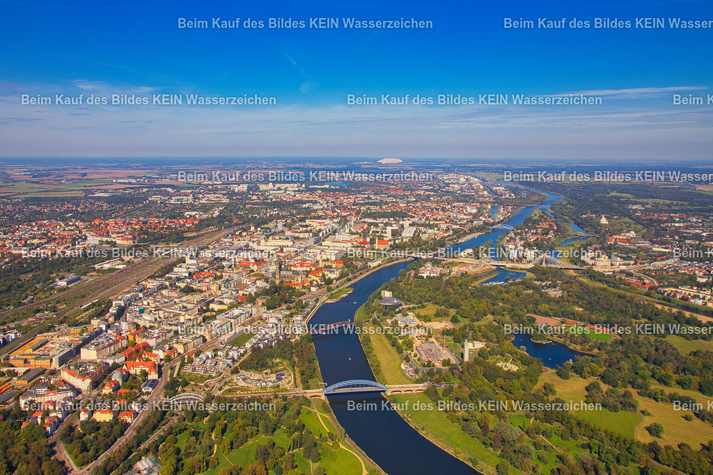Panorama über die Landeshauptstadt Magdeburg | Aus großer Höhe eröffnet sich ein weitreichender Blick über die gesamte Landeshauptstadt Magdeburg. Die Elbe durchzieht das Panorama als prägende Lebensader der Stadt und trennt die historische Innenstadt vom weitläufigen Stadtpark Rotehorn mit dem Adolf-Mittag-See. Links des Flusses erstreckt sich das Stadtgebiet vom Hasselbachplatz über die Altstadt, Neue Neustadt und den Kannenstieg, während am westlichen Bildrand die Eisenbahntrassen und der Stadtteil Stadtfeld zu erkennen sind. Am Horizont zeichnet sich die Kalihalde bei Zielitz, der „Kalimandscharo“, ab. Die Luftaufnahme vermittelt die räumliche Struktur Magdeburgs und bildet einen eindrucksvollen Abschluss des fotografischen Rundgangs durch die Landeshauptstadt. - Realisiert mit Pictrs.com
