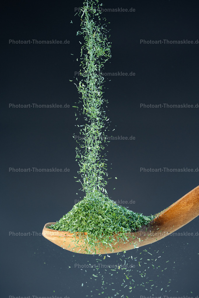 Getrocknete Dillspitzen – Aromatische Kräuter für feine Speisen | Getrocknete Dillspitzen – Aromatische Kräuter für feine Speisen. Kollektion: A spoon of tastefully seasoningsInhalt:Fein geschnittener getrockneter Dill schwebt in einem lebhaften, fast magischen Strom in einen Holzlöffel. Die zarten Kräuterflocken wirbeln in der Luft, als wären sie ein grüner Nebel – voller Leben, Frische und Aroma. Das Bild fängt den Moment der Leichtigkeit ein, in dem das Gewürz zu tanzen scheint, bevor es sich sanft niederlässt.Farben:Hintergrund: Ruhiges, tiefes Grau-Blau – schlicht, um die leuchtende Farbe des Dills hervorzuheben.Dill: Intensives Smaragdgrün, das an Frische, Natur und kulinarische Raffinesse erinnert.Löffel: Warme Holztöne mit sichtbarer Maserung – natürlich, erdig, vertraut.Stil:Sanft, poetisch und lebendig. Die Darstellung der feinen Dillspitzen in Bewegung erzeugt eine fast hypnotische Ruhe und bringt das Gefühl von Frische und Natürlichkeit in den Vordergrund.Ideale Orte zum Aufhängen:Kräuterküche oder -gartenbereich: Für Liebhaber frischer, grüner Aromen.Feinkostgeschäft oder Bio-Laden: Symbolisiert die Kraft der Natur in ihrer feinsten Form.Therapie- oder Aromatherapie-Räume: Dill hat eine beruhigende Wirkung – das Bild wirkt ebenfalls entsprechend.Skandinavisch inspirierte Wohnräume: Die Farbtöne und Schlichtheit passen wunderbar zu nordischen Designs. - Realisiert mit Pictrs.com