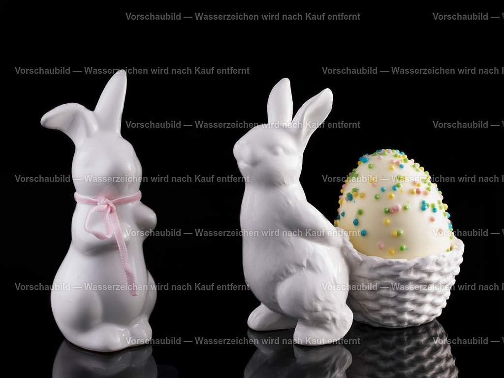 Zwei porzelan Osterhasen mit einen weissen, verzierten Schaumkuss Osterei im Korb | Zwei porzellan Osterhasen mit einen weissen, verzierten Schaumkuss Osterei im Korb - Realisiert mit Pictrs.com