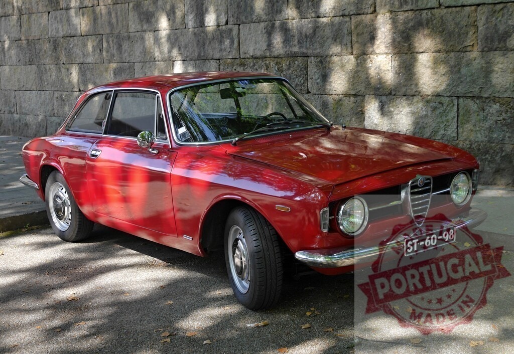 Alfa Romeo red vintage sports car parked by wall | Red classic Alfa Romeo coupe parked on asphalt beside a stone wall - Realized with Pictrs.com