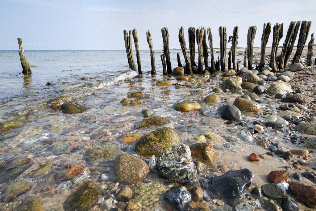 Gänsemarsch der Holzfiguren | Wie im Gänsemarsch scheinen hölzerne Gestalten an einem steinigen Strand hintereinander ins Wasser zu laufen.