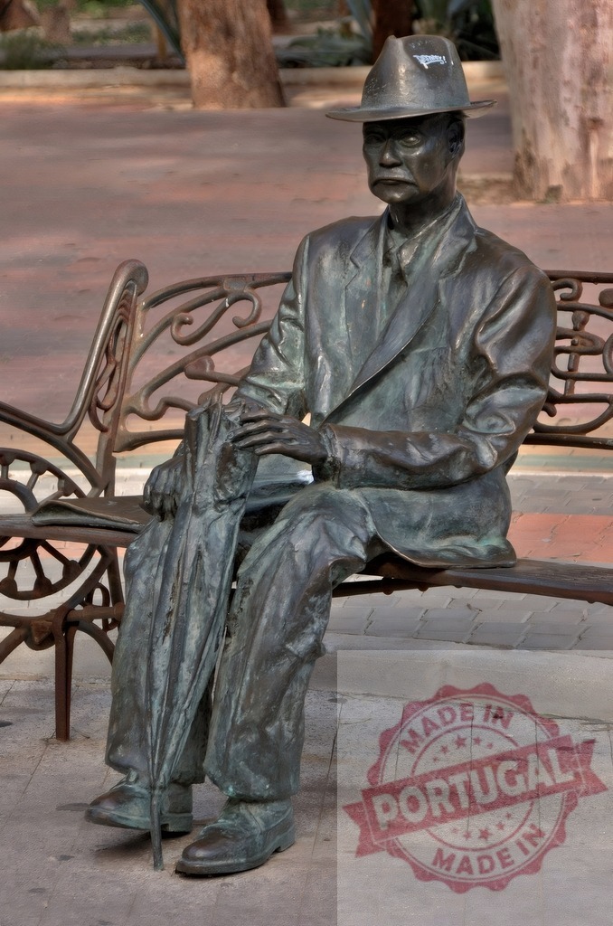 Bronze statue of man sitting on park bench | Bronze statue of an old man with a hat and umbrella sitting on a bench in a public park - Realized with Pictrs.com