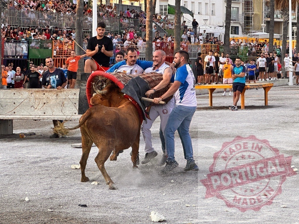 People carrying a large basket while interacting with a bull during a festival | Men working together to lift a heavy basket, trying to avoid a charging bull during a Spanish festival event - Realized with Pictrs.com