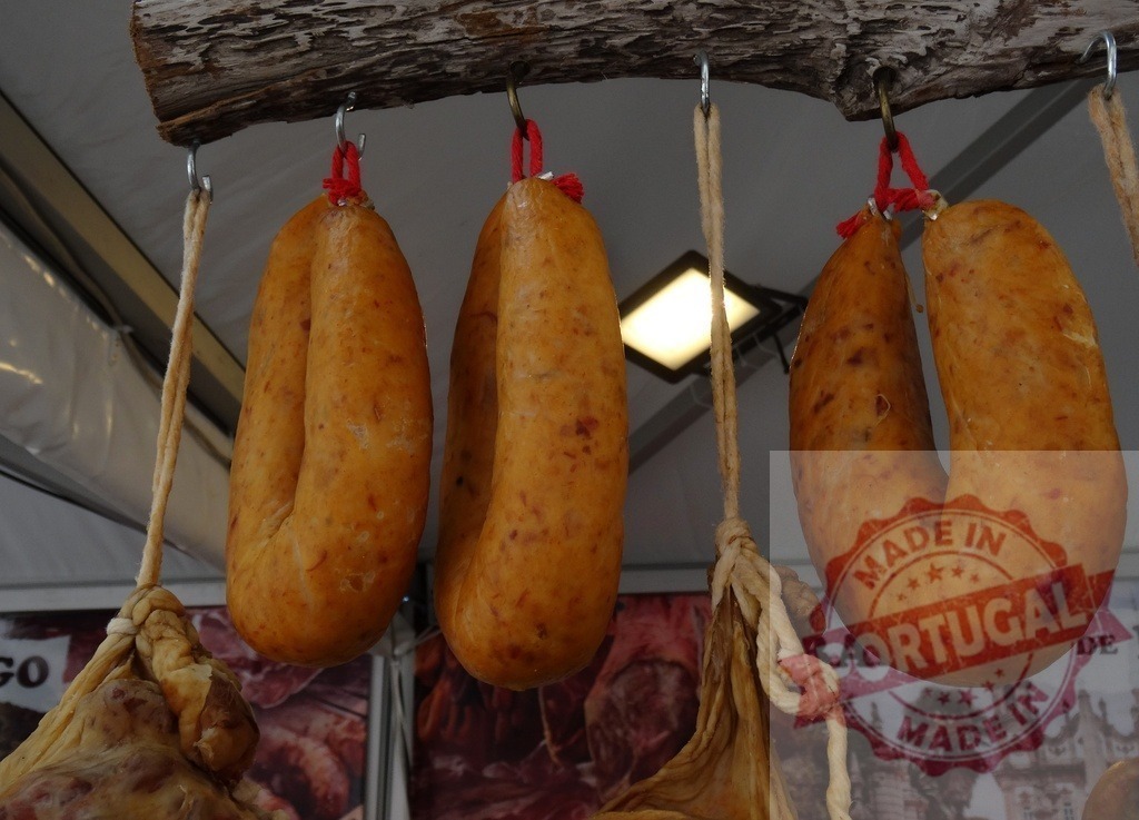 Chorizo sausages hanging at a traditional street market | Cured chorizo sausages hanging from a wooden beam at a food market - Realisiert mit Pictrs.com
