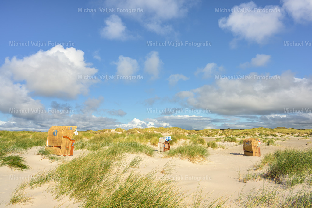 Strandkörbe in den Dünen auf Amrum | Strandkörbe, die traditionellen deutschen Strandstühle, sind ein charakteristisches Merkmal der Küstenlandschaft und bieten Schutz vor Wind und Sonne. Auf der Nordseeinsel Amrum, bekannt für ihre malerischen Dünenlandschaften, sind diese Körbe ein beliebter Rückzugsort für Besucher, die die ruhige Atmosphäre und die atemberaubende Aussicht genießen möchten. In den Dünen verstreut, schaffen sie eine einzigartige und gemütliche Umgebung, um die natürliche Schönheit der Insel in vollen Zügen zu erleben. - Realisiert mit Pictrs.com