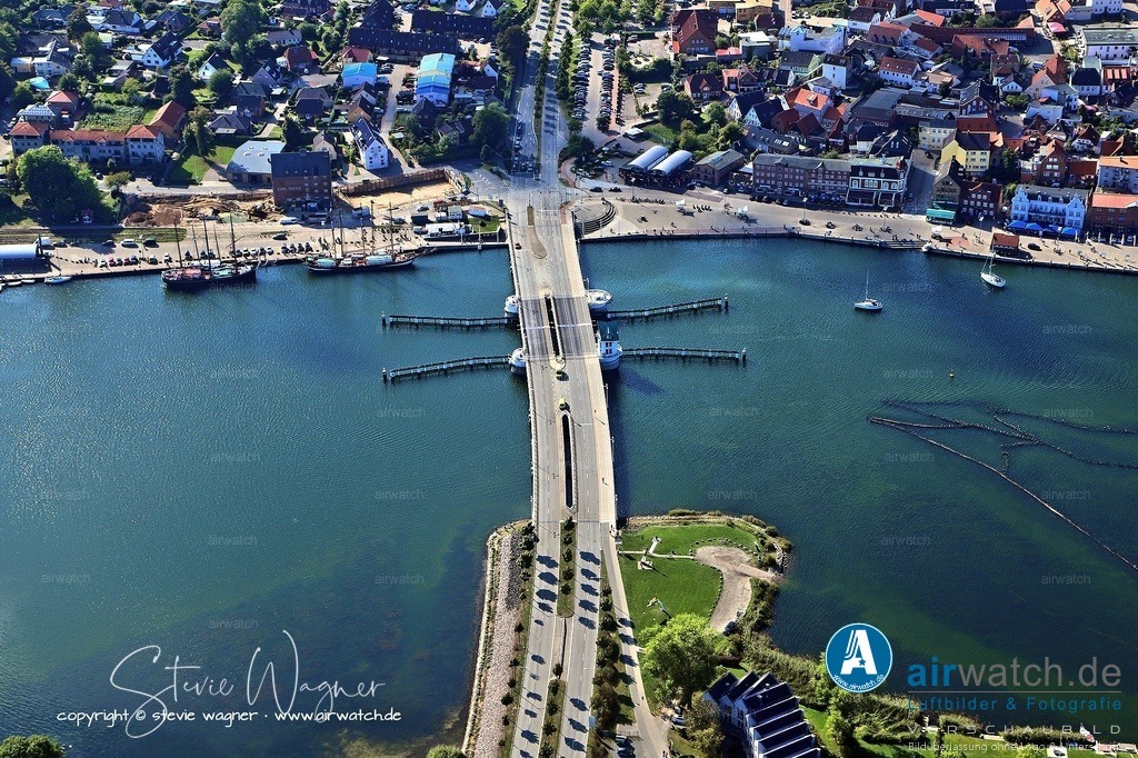 Luftbild Kappeln an der Schlei - Die Brücke ersetzte die vorherige Drehbrücke, die ab 2003 abgerissen wurde. | Die Brücke ersetzte die vorherige Drehbrücke, die ab 2003 abgerissen wurde. Seit 2022 gab es kurzfristige Bauarbeiten aufgrund einer Schadensanalyse. Im März 2025 fanden reguläre Jahreswartungen statt, wobei jeweils eine Klappe gesperrt war und der Verkehr einspurig mit 30 km/h geführt wurde. Während dieser Zeit waren Sonderöffnungen für Schiffe nach vorheriger Anmeldung beim Brückenwärter möglich.