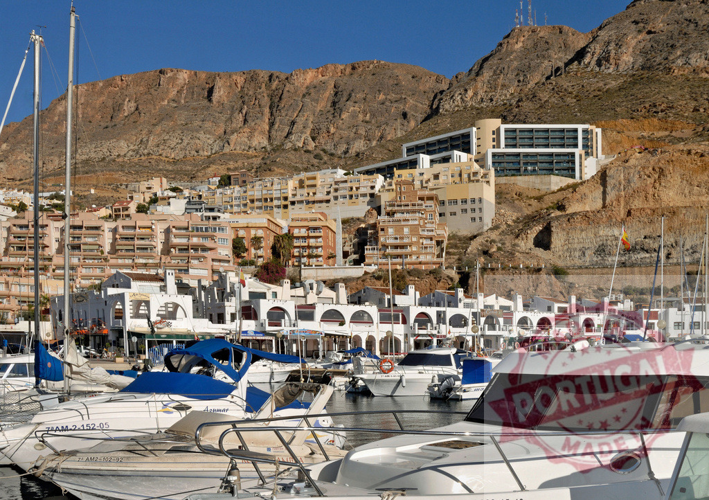 Boats mooring in a marina with hillside architecture in Spain | Boats are moored in a sunny Spanish marina with buildings climbing up a dry hillside - Realisiert mit Pictrs.com