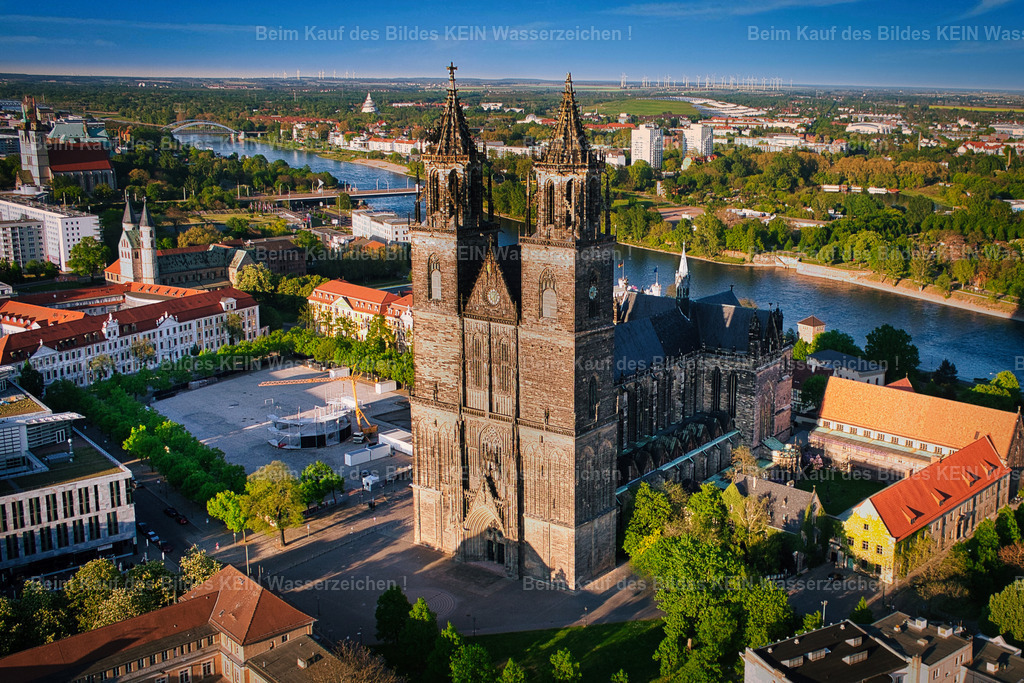 Magdeburg_Luftbild_Dom_2016_Domplatz_Elbe_6661_GEN | Dieses Luftbild zeigt den Magdeburger Dom an einem sonnigen Tag aus einer eindrucksvollen Perspektive über der Elbe. Die Aufnahme entstand bereits im Jahr 2016 und wurde nun erneut digital bearbeitet, um die Details, Farben und die besondere Atmosphäre des Motivs noch stärker hervorzuheben.Die Elbe führt den Blick des Betrachters direkt auf das Hauptmotiv, den Magdeburger Dom. Als älteste gotische Kathedrale Deutschlands prägt das Bauwerk seit Jahrhunderten die Silhouette der Landeshauptstadt Sachsen-Anhalts. Aus der Vogelperspektive wird die besondere Lage des Doms am Elbufer sowie seine Einbindung in das historische Stadtzentrum besonders deutlich sichtbar.Das sonnige Wetter sorgt für klare Konturen und eine hohe Detailtiefe. Die neu überarbeitete Bildbearbeitung verleiht der Aufnahme zusätzliche Brillanz und betont die harmonische Verbindung zwischen Flusslandschaft, historischer Architektur und urbanem Raum.Dieses Luftbild dokumentiert nicht nur eines der bedeutendsten Wahrzeichen Magdeburgs, sondern zeigt auch die zeitlose Schönheit der Stadt aus einer Perspektive, die nur aus der Luft erlebbar ist. - Realisiert mit Pictrs.com