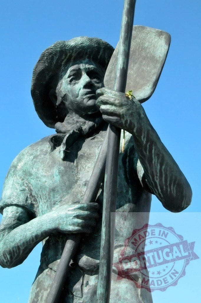 Bronze man statue holding paddle against blue sky | Bronze statue of a man wearing a hat and holding a paddle, standing against a clear blue sky - Realisiert mit Pictrs.com