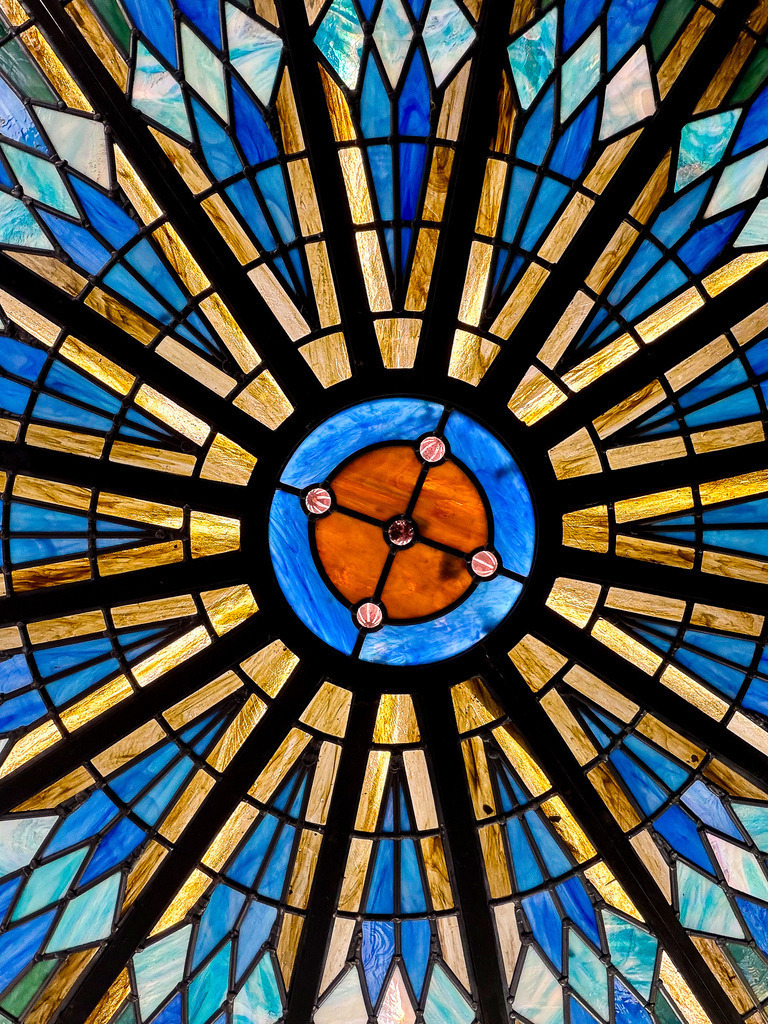 Kaleidoskop der Architektur: Symmetrische Glasmalerei | Ein zeitloses Meisterwerk aus Licht, Farbe und vollendeter Geometrie. Diese faszinierende Fine-Art-Fotografie fängt das hypnotische, radiale Symmetrie-Muster einer historischen Glaskuppel ein. Das prachtvolle Zusammenspiel aus tiefem Saphirblau, feurigem Orange und strahlenden Goldtönen erinnert an ein lebendiges Kaleidoskop. Sobald Licht auf dieses Motiv trifft, entfaltet es eine fast sakrale, beruhigende und zugleich kraftvolle Atmosphäre im Raum. Ein exklusiver Blickfang für anspruchsvolle Wohnkonzepte. Bringt maximale Farbbrillanz und Tiefe als High-End-Acrylglas-Print, der das Licht wie echtes Glas bricht. - Realisiert mit Pictrs.com