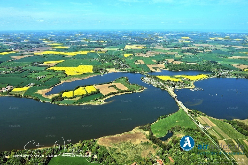 Luftbild Ostseefjord Schlei, Gunnebyer Noor, Badestrand Gunneby, Landschaftsschutzgebiet Schwansener Schleilandschaft, Schneiderhaken, Lindaunisbrücke | Schneiderhaken, Lindaunisbrücke: Der Schleistrand Schneiderhaken in Lindaunis, einer Gemeinde im Kreis Schleswig-Flensburg, ist eine beliebte Badestelle mit Blick auf die historische Lindaunisbrücke, die die Regionsteile Schwansen und Angeln verbindet. Der Strand, der zu den kleineren Sandstränden an der Schlei gehört, bietet eine Liegewiese, Sitzmöglichkeiten, einen Kinderspielplatz mit Grillstelle