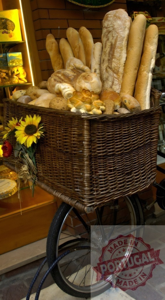 Bicycle basket displaying various fresh baked bread loaves | Wicker basket on a vintage bicycle filled with an assortment of fresh bread and sunflowers - Realized with Pictrs.com
