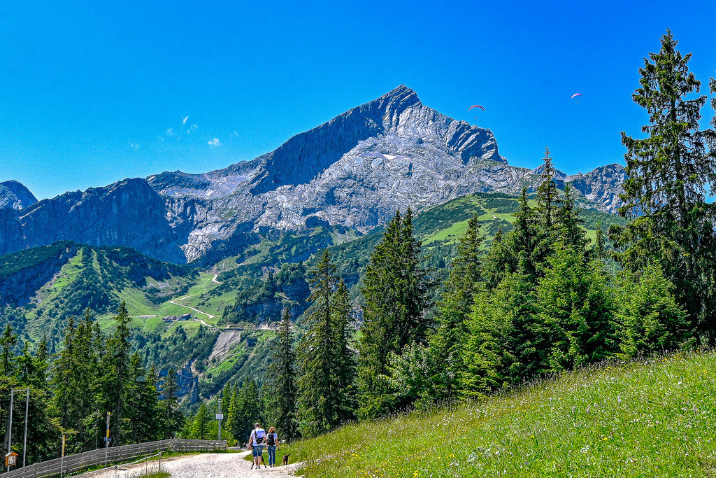 Faszination Alpen: Gipfelsturm und Freiheit | Ein atemberaubender Anblick, der die Sehnsucht nach den Bergen weckt: Majestätisch und unbezwingbar ragt die markante Pyramidengestalt der Alpspitze in den strahlend blauen Himmel empor. Ihre steilen Felswände und bizarren Grate erzählen von jahrtausendealter Erdgeschichte und der rohen Kraft der Natur. Zwei Gleitschirmflieger, winzige Punkte vor der gewaltigen Kulisse, unterstreichen die Dimensionen und die unendliche Weite der Bergwelt. Dieses Bild ist eine Hommage an die Schönheit der Alpen und den Traum von Freiheit und Abenteuer. - Realisiert mit Pictrs.com
