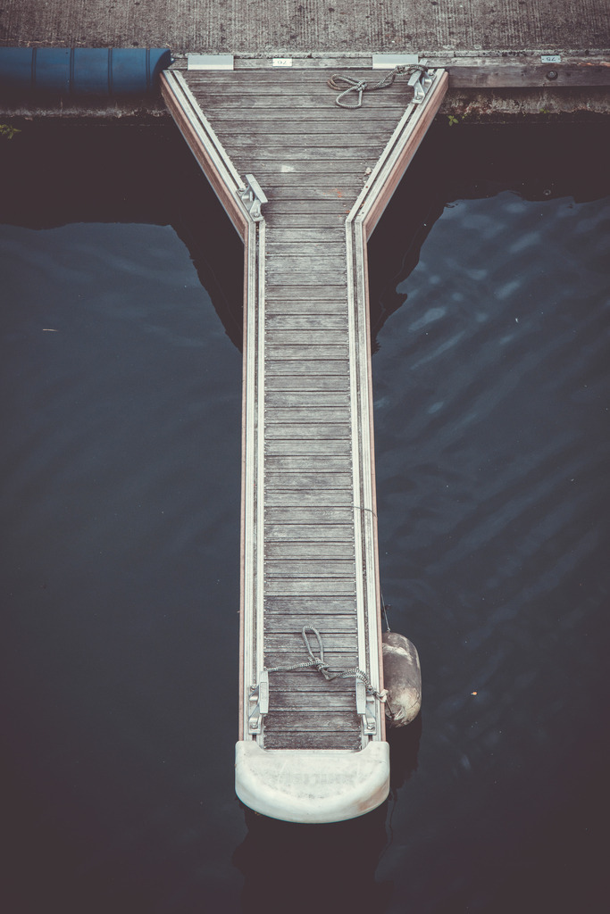 Stillness at the Dock | Ein einzelner Steg ragt in das dunkle Wasser und wird aus der erhöhten Perspektive zu einer nahezu abstrakten, minimalistischen Komposition.Die klare Geometrie des Stegs steht im Kontrast zur ruhigen, leicht strukturierten Wasseroberfläche. Gedämpfte Blau- und Grautöne verleihen der Aufnahme eine zurückhaltende, atmosphärische Stimmung und unterstreichen den Fine-Art-Charakter des Motivs.Ein ruhiges maritimes Wandbild für moderne und minimalistische Räume – reduziert auf Form, Struktur, Wasser und Stille. - Realisiert mit Pictrs.com