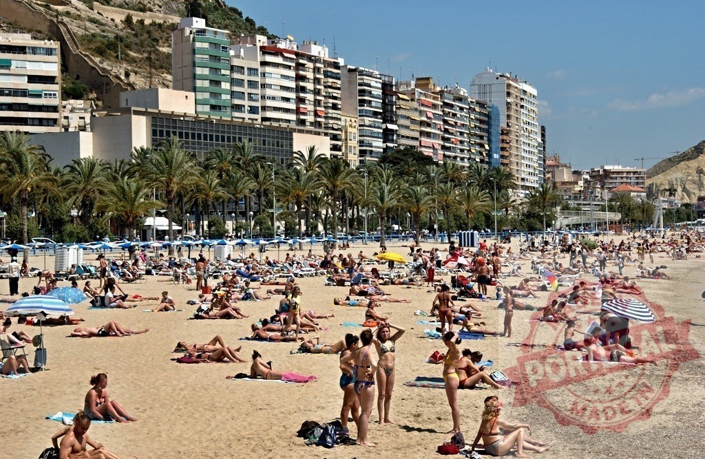 Crowded Postiguet beach in Alicante Spain during summer vacation | People enjoying a sunny day, sunbathing on the sand with city buildings in the background - Realisiert mit Pictrs.com