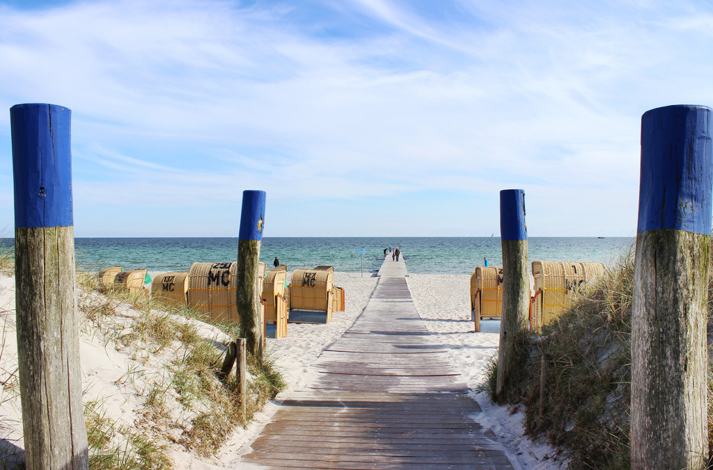 Wandbild: Südstrand Burgtiefe auf der Insel Fehmarn | Dieses Wandbild im Querformat zeigt einen schönen Weg am Südstrand auf Fehmarn. Auf dem Strand befinden sich zahlreiche Strandkörbe. Am blauen Himmel sind viele Schleierwolken zu sehen.  - Realisiert mit Pictrs.com