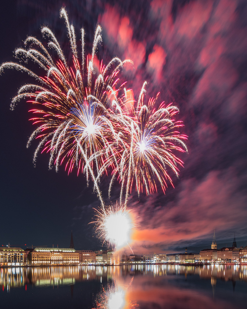 Lichtermeer über Hamburg | Zahlreiche Feuerwerkskörper entfalten sich gleichzeitig über der Hamburger Alster. Rote, weiße und goldene Lichtspuren dominieren die spektakuläre nächtliche Szene. - Realisiert mit Pictrs.com