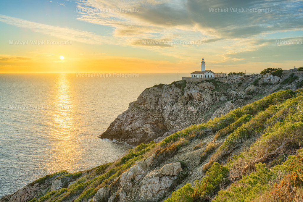 Goldenes Licht am Faro de Capdepera auf Mallorca | Der Faro de Capdepera steht im warmen Licht der aufgegangenen Sonne, die die Klippen in ein kräftiges Gold taucht und ihre Struktur klar hervorhebt. Die Felsformationen wirken durch das Morgenlicht plastisch und lebendig, während das Meer darunter ruhig bleibt und die warmen Töne dezent aufnimmt. Der Leuchtturm fügt sich sichtbar in diese Küstenlandschaft ein, ohne sie zu dominieren – die Szene lebt vor allem von der Kombination aus rauer Felsküste, offenem Meer und dem intensiven, warmen Licht des frühen Tages. - Realisiert mit Pictrs.com