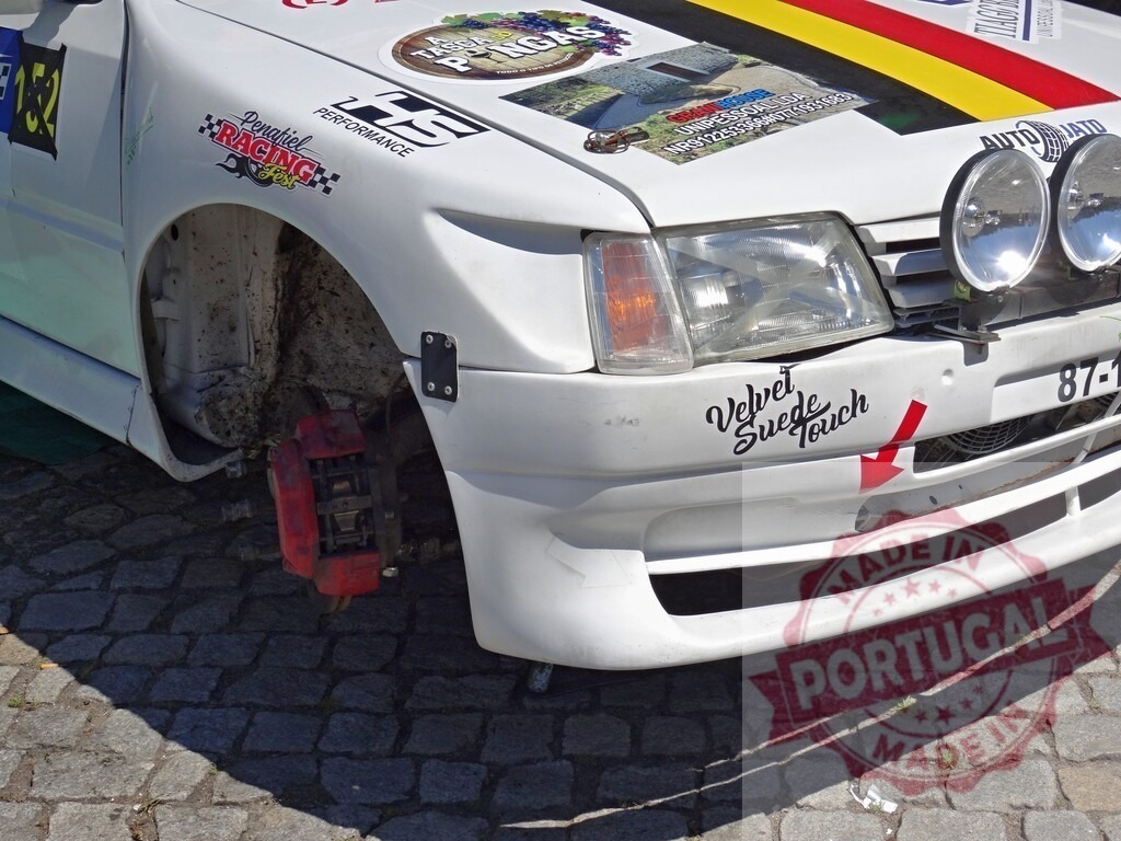 Rally car Peugeot 205 under service with exposed brake | Rally car Peugeot 205 with removed wheel getting maintenance on brake caliper - Realized with Pictrs.com