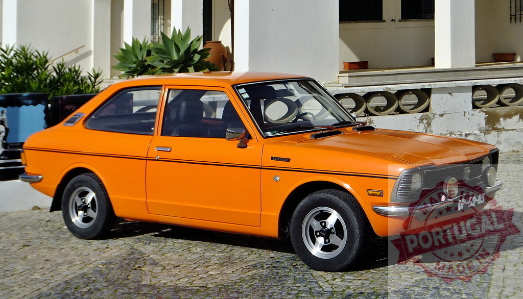 Orange Toyota Corolla parked in cobblestone square | Classic orange Toyota Corolla parked in front of a white building with plants in pots - Realized with Pictrs.com
