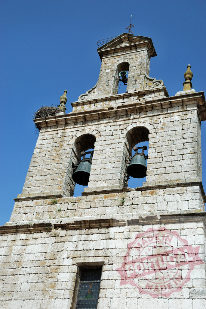 Ancient church stone bell tower with stork nest. Spain - Burgos | Stone bell tower with bronze bells and a stork nest under a clear blue sky - Realized with Pictrs.com
