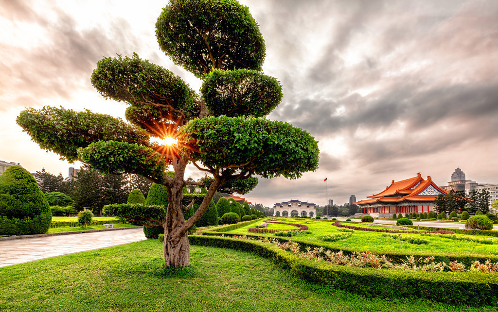 0Y9A8017-Verbessert-RR-Bearbeitet Kopie_neu Kopie | Das Bild zeigt den Freiheitsplatz (Liberty Square) mit Blick auf die Gebäude im Bereich der Chiang-Kai-shek-Gedächtnishalle in Taipeh, Taiwan.Taipeh, die Hauptstadt von Taiwan.Vordergrund: Ein kunstvoll in Form geschnittener Zierbaum (Bonsai-Stil) auf einer gepflegten Rasenfläche.Die traditionelle chinesische Architektur der Konzerthalle oder des Theaters mit ihren charakteristischen orangen Dächern.Die Abendsonne bricht durch die Äste des Baumes und sorgt für eine warme, stimmungsvolle Beleuchtung - Realisiert mit Pictrs.com