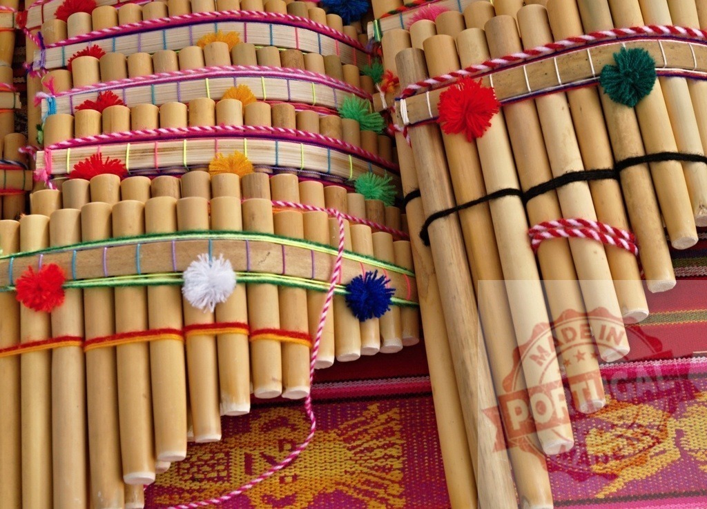 Colorful Andean panpipes laying on a vibrant textile, representing Peruvian culture and music | Traditional Andean panpipes, adorned with colorful yarn and pompoms, rest on a vibrant textile, showcasing Peruvian craftsmanship and musical heritage - Realisiert mit Pictrs.com
