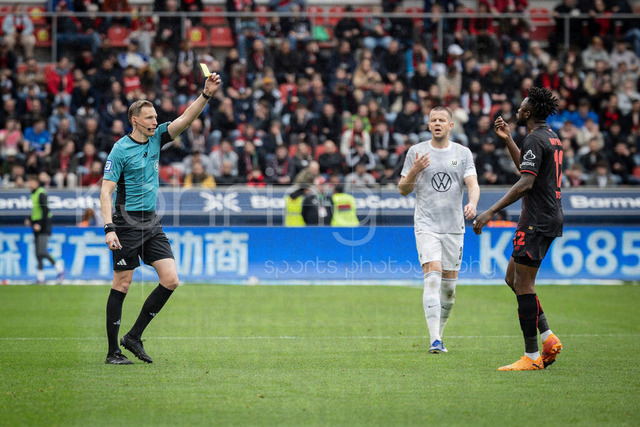 German Bundesliga, Bayer 04 Leverkusen vs. VfL Wolfsburg, 04.04.2026 | LEVERKUSEN, GERMANY - APRIL 4, 2026 :  referee Martin Petersen (Stuttgart) is showing Edmond Tapsoba (Bayer 04 Leverkusen, 12) a yellow card after a foul in the box causing a penalty, Denis Vavro (VfL Wolfsburg, 3) in the background during the German Bundesliga match on gameday 28 between Bayer 04 Leverkusen vs. VfL Wolfsburg at BayArena on April 4, 2026 in Leverkusen, Germany. DFL REGULATIONS PROHIBIT ANY USE OF PHOTOGRAPHS AS IMAGE SEQUENCES AND/OR QUASI-VIDEO.