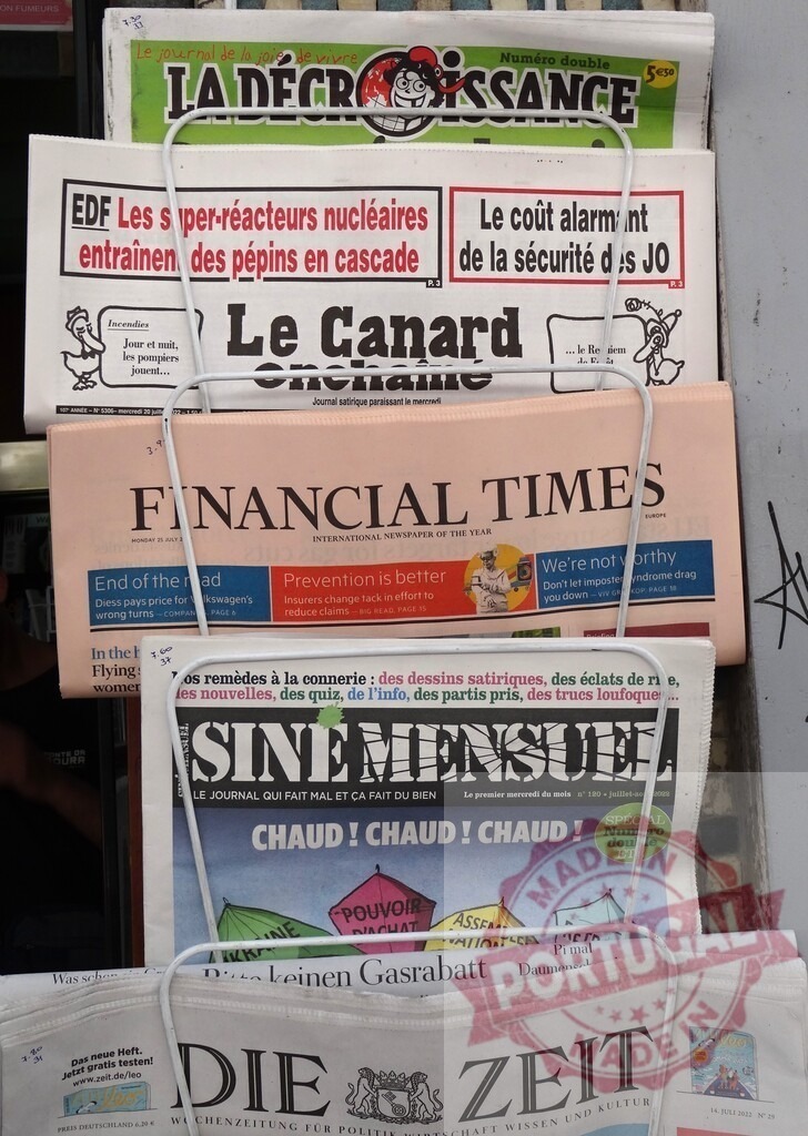 Selection of French and international newspapers displayed on a newsstand, offering diverse perspectives on current events | International newspapers La Décroissance, Le Canard Enchaîné, Financial Times, Siné Mensuel and Die Zeit displayed on newsstand - Realized with Pictrs.com