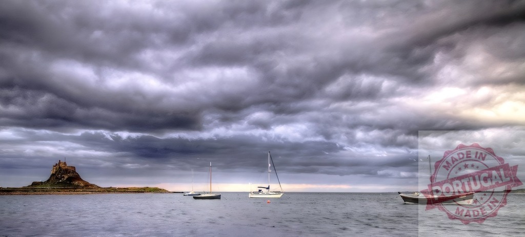Lindisfarne Castle with sailboats under stormy sky, Holy Island | Lindisfarne Castle standing on an island with sailboats anchored in calm water under cloudy sky - Realisiert mit Pictrs.com
