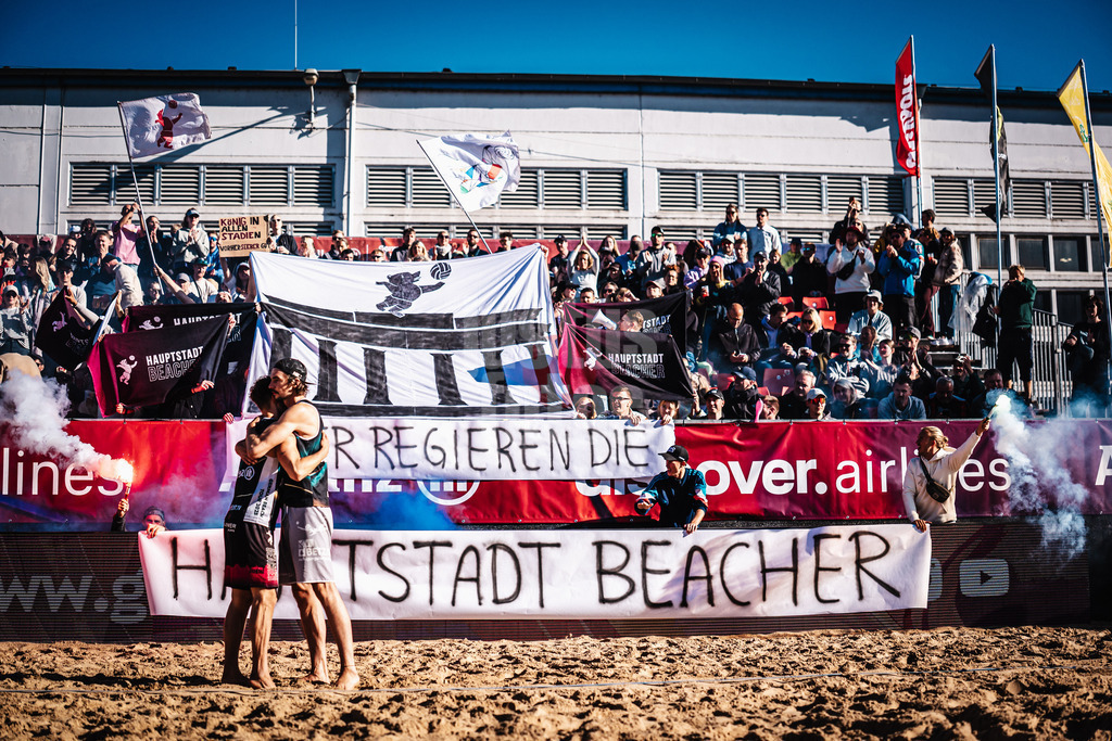 Beachvolleyball | Männer | Allianz German Beach Tour 2025 | Tourstop Berlin | 23.08.2025 | Einlauf von v.l. Eric Stadie-Seeber und Jannik Kühlborn, im Hintergrund die Fangruppe Fraktion Bräune mit einer Choreo und Pyrotechnik, Hier Regieren Die Hauptstadt Beacher
