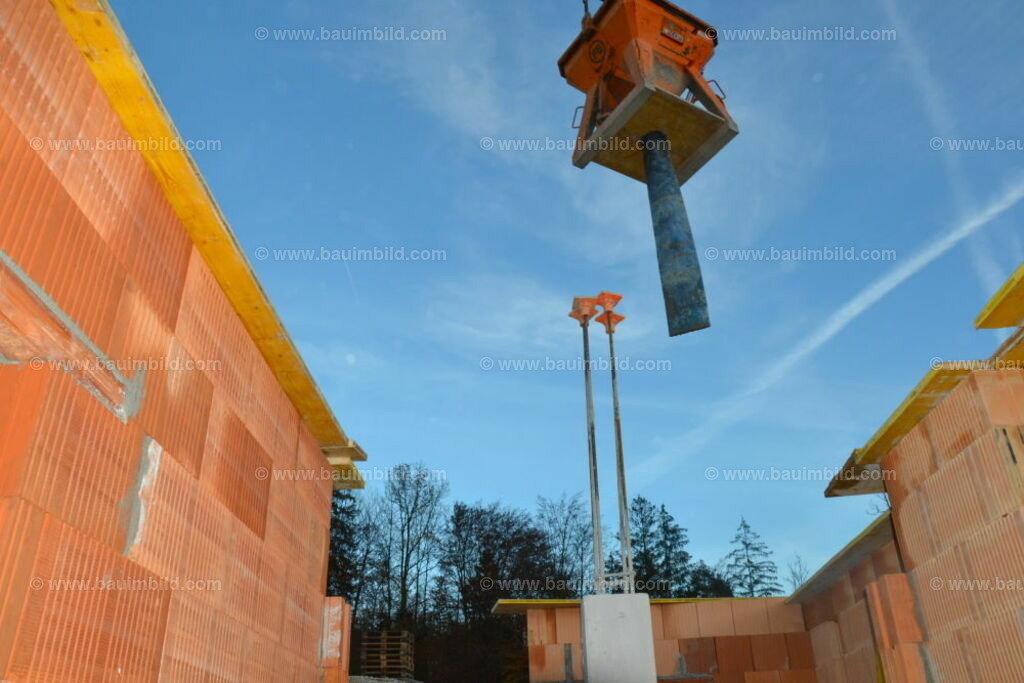 Krankübel mit Schlauch  | Über Ziegelmauern schwebender Krankübel mit Schlauch für Betoneinbau, Hintergrund blauer Himmel