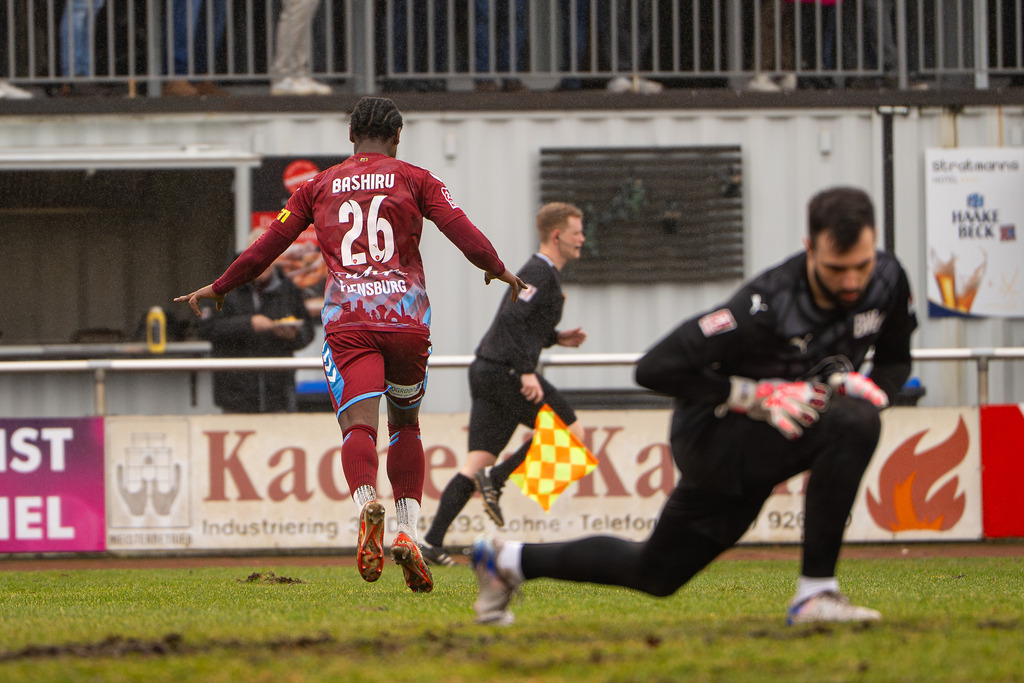 Fußball I Herren I Saison 2025-2026 I Regionalliga Nord I 23. Spieltag I TuS Blau-Weiß Lohne - SC Weiche Flensburg 08 I 0042 | Ibrahim Bashiru Ali (26, SC Weiche Flensburg 08) jubelt im Rücken von Marko Dedovic (1, TuS BW Lohne) - Realisiert mit Pictrs.com
