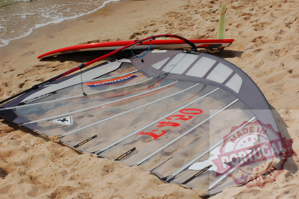 Windsurfing sail and board lying on sandy beach near seashore | Windsurfing equipment left on the beach after a session, suggesting a relaxing break from watersports - Realisiert mit Pictrs.com